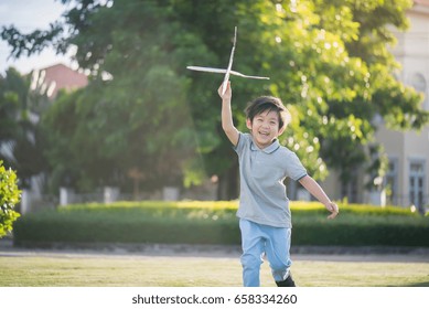 Cute Asian Child Playing Cardboard Airplane In The Park Outdoors