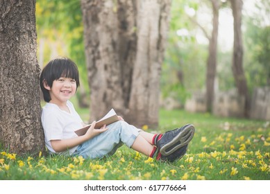 Cute Asian Child Reading A Book Under The Tree