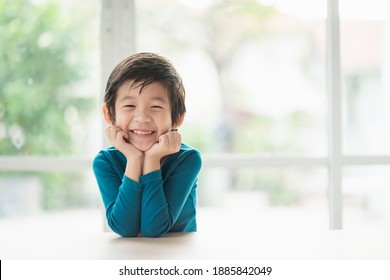 Cute Asian child resting chins on hands on wood table with copy space on right