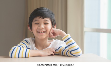 Cute Asian child resting chins on hands on wood table