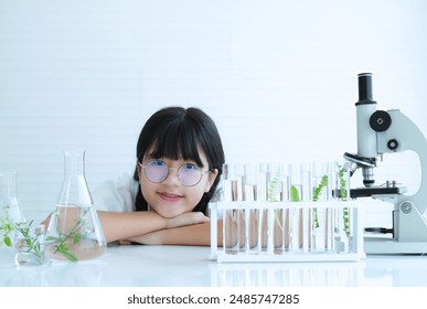 Cute asian child scientist lie with your chin resting on your arm with green leaf in many test tubes and a microscope at science laboratory and research biotechnology. - Powered by Shutterstock