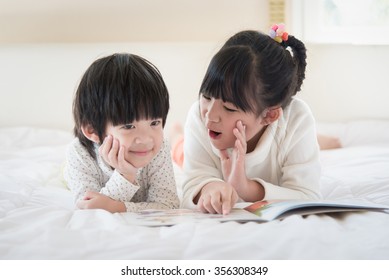 Cute Asian Children Reading Book On White Bed