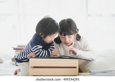 Cute Asian Children Reading A Book On White Bed