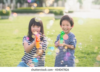 Cute Asian Children Shooting Bubbles From Bubble Gun In The Park