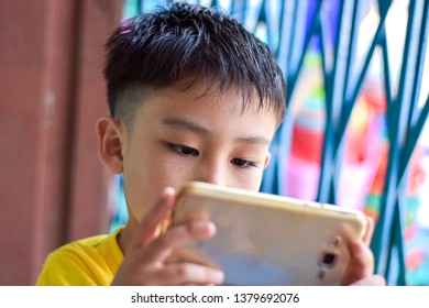 Cute Asian Chinese Boy With Squint Eyes Playing Mobile Game On Smartphone That Shows Eye Damage Or Eye Strain