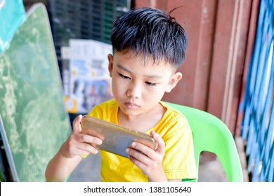 Cute Asian Chinese Boy With Squint Eyes Playing Mobile Game On Smartphone That Shows Eye Damage Or Eye Strain