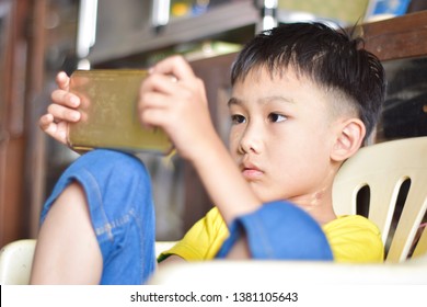 Cute Asian Chinese Boy With Squint Eyes Playing Mobile Game On Smartphone That Shows Eye Damage Or Eye Strain