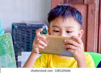 Cute Asian Chinese Boy With Squint Eyes Playing Mobile Game On Smartphone That Shows Eye Damage Or Eye Strain