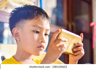 Cute Asian Chinese Boy With Squint Eyes Playing Mobile Game On Smartphone That Shows Eye Damage Or Eye Strain