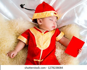 Cute Asian Four-month Baby In Chinese Traditional Red Dress Sleeping With Red Envelope Of Money Gift  In Chinese Newyear Festival. Happy Chinese New Year Concept.