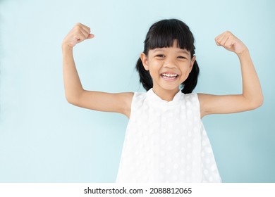 Cute Asian  girl, 4 to 6 years old, black hair, white sleeveless shirt. She clenched her fists and raised both of her arms.To show the muscles in the arms and their strength with a happy smiling face.