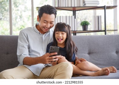 Cute asian girl help young father show something on smartphone making selfie together, smart daughter and dad sit on couch hold mobile phone take family picture on moblie phone. - Powered by Shutterstock