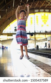 A Cute Asian Girl Jumping For Joy On The Side Of A Train Track At A Train Station. 