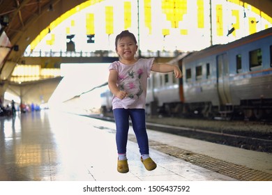 A Cute Asian Girl Jumping For Joy On The Side Of A Train Track At A Train Station. 