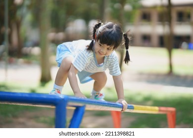 Cute Asian Girl Smile Play Climb The Bar On School Or Kindergarten Yard Or Playground. Healthy Activity Children. Little Girl Climbing Outdoors At Playground. Child Playing On Outdoor Playground.