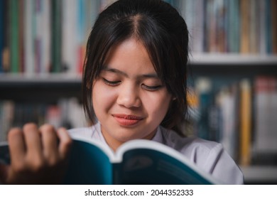 Cute Asian Girl Student Reading A Book At Her School In The Library. Close Up