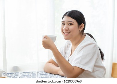 Cute Asian Girl Teen Sitting At Home Hand Hold White Cup Mug And Smile For Diet Drinking Herbal Tea Or Healthy Drink.