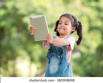 A Cute Asian Girl Is Using A Tablet For Fun Playing Games And Learning Outside Of School In The Park