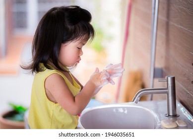 Cute Asian girl washed her hands with soap in the white sink. Children rub the bubbles in her hands intently. Side view of kids was cleaning her palms to wash away the dirt. Child is 3-4 years old.