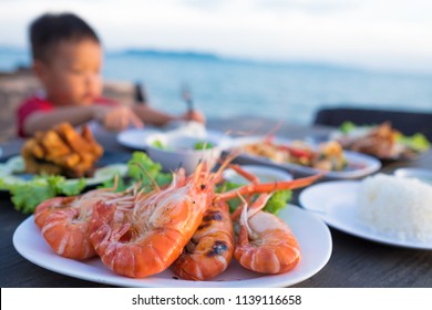 Cute Asian Kid Boy Eating  Various Seafood At Dinner Table By Self.  Foods At The Beach. Selective Focus.