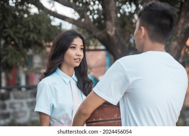 A cute asian lady has a serious conversation with her slacker boyfriend holding an old basketball.