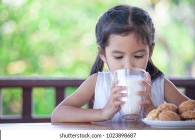 Cute Asian Little Child Girl Is Drinking A Milk From Glass With Cookies For Breakfast