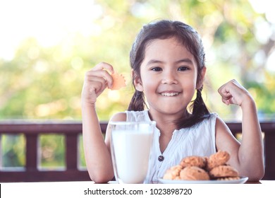 Dễ thương châu á bé gái làm bàn tay mạnh mẽ trong khi uống một sữa cho bữa ăn sáng với niềm vui