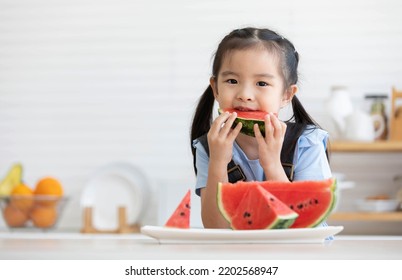 Cute Asian Little Child Girl Eating Slice Watermelon In The Kitchen