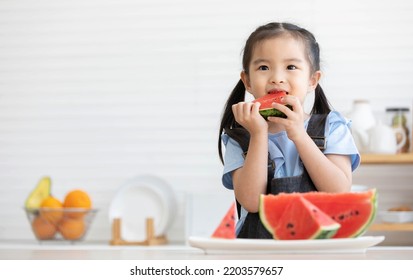 Cute Asian Little Child Girl Eating Slice Watermelon In The Kitchen