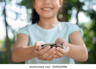 Cute Asian Little Girl Playing With Coins Money, Child Hand Holding Money. Kid Saving Money Into Piggy Bank. Child Counting His Saved Coins, Children Learning About For The Future Concept.