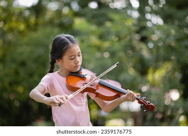 Cute Asian little girl playing the violin in the park, education music concept - Powered by Shutterstock