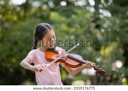 Cute Asian little girl playing the violin in the park, education music concept