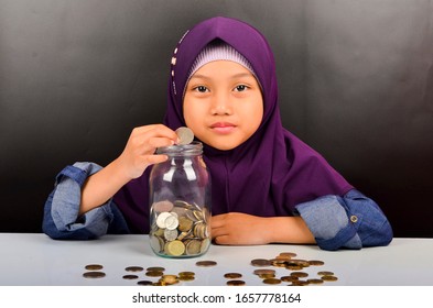 Das süße asiatische Mädchen trägt Hijab und spielt mit Münzen. Geld sparen für das Zukunftskonzept.