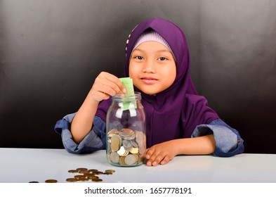 Das süße asiatische Mädchen trägt Hijab und spielt mit Münzen. Geld sparen für das Zukunftskonzept.