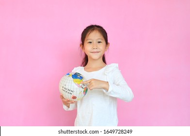 Cute Asian Little Kid Girl Holding A Globe With Pointing United States At Map On Earth Isolated Over Pink Background. Portrait Of Child With The Earth Globe Sphere. Focus At Children Face.