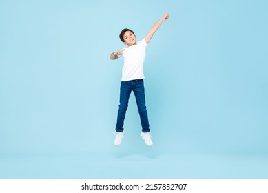 Cute Asian mixed race boy jumping with hand pointing up in isolated light blue color studio background