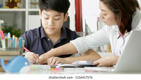 Cute asian mother helping your son doing your homework at home with smile face together.