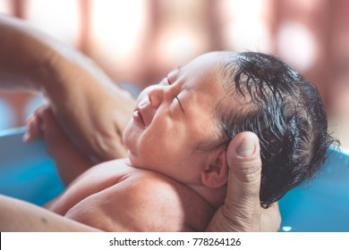 Cute Asian Newborn Baby Girl Take A Bath In Bathtub. Mom Cleaning Her Baby Body With Tenderness