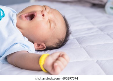 Cute Asian Newborn Yawn While Lying On The Soft White Bed In The Time That Needed Rest At Home. Adorable Baby While Sleeping During A Memorable Family Moment. Concept Of Breastfeeding Development