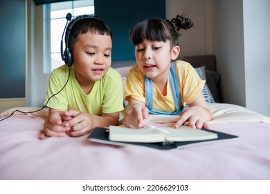 Cute Asian Older Sister Teach Brother Reading Book. Brother Using Headphone.