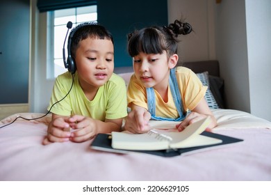 Cute Asian Older Sister Teach Brother Reading Book. Brother Using Headphone.