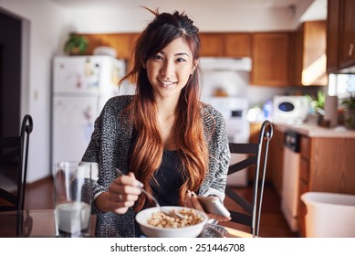 Cute Asian Teen Girl Eating Breakfast In Kitchen With Smart Phone