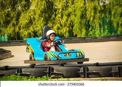 Cute Asian Thai Girl Is Driving Go-kart Car With Speed In A Playground Racing Track. Go Kart Is A Popular Leisure Motor Sports.