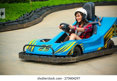 Cute Asian Thai Girl Is Driving Go-kart Car With Speed In A Playground Racing Track. Go Kart Is A Popular Leisure Motor Sports.