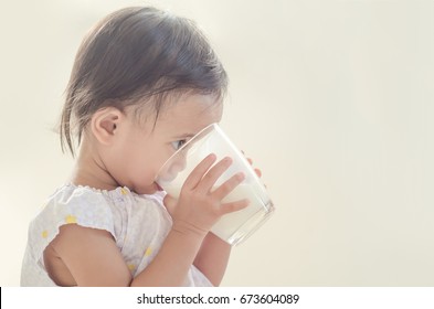 Cute Asian Toddler Girl Drinking Milk From Big Glass On White Background.