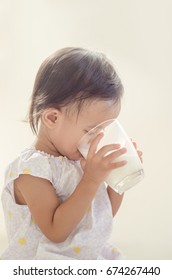 Cute Asian Toddler Girl Drinking Milk From Big Glass On White Background.