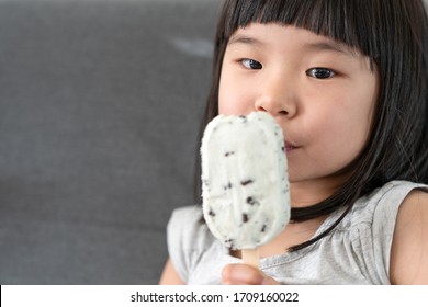 Cute Asian Toddler Girl Eating Ice Cream On Couch