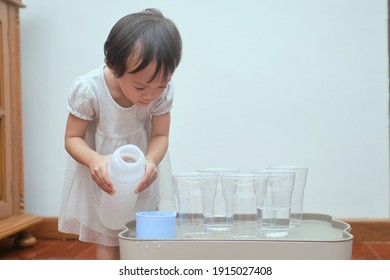 Cute Asian Toddler Girl Having Fun Playing With Water Table At Home, Wet Pouring Montessori Preschool Practical Life Activities, Fine Motor Skills Development, Stay Home Stay Safe Have Fun Concept