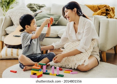 Cute Asian Woman And Kid Playing Educational Toys Together In Living Room. Mom And Son Play Cubes And Laugh Happy Family. Young Mother And Son Doing Activities Together At Home.