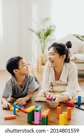 Cute Asian Woman And Kid Playing Educational Toys Together In Living Room. Mom And Son Play Cubes And Laugh Happy Family. Young Mother And Son Doing Activities Together At Home.